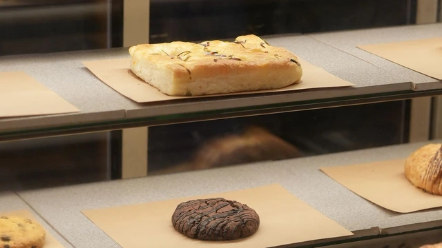 Vitrine de padaria com prateleiras de vidro, focaccia e cookie de chocolate sobre papel pardo, em luz suave